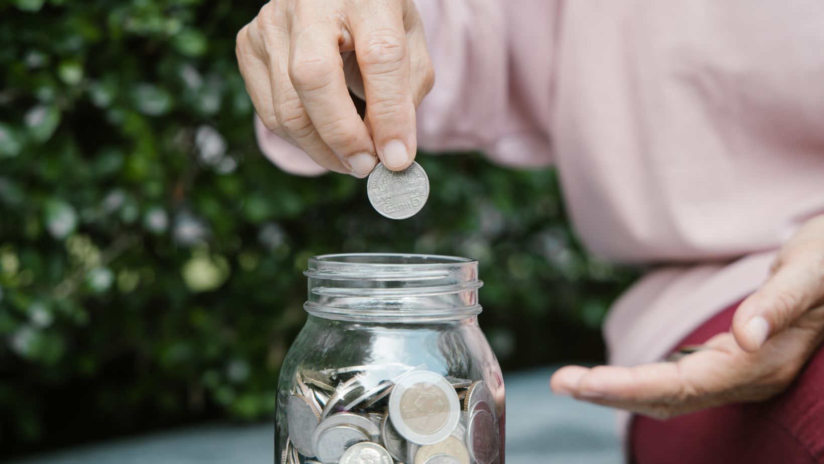 a hand putting coins into a mason jar